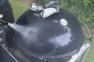 man washing charcoal grill with power washer